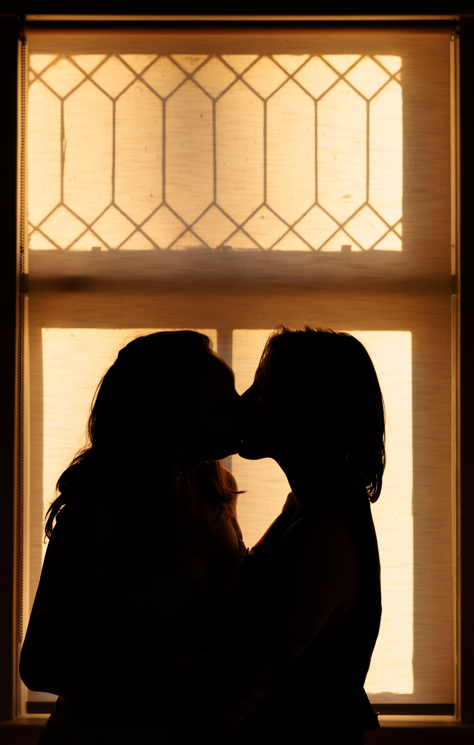 Newlyweds kiss, silhouetted by golden window light.